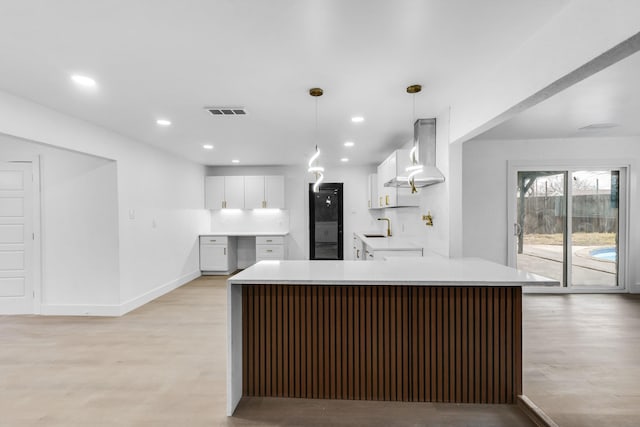 kitchen with pendant lighting, white cabinetry, sink, kitchen peninsula, and wall chimney range hood