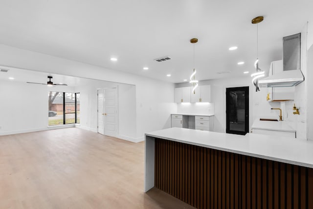 kitchen with wall chimney exhaust hood, sink, hanging light fixtures, light wood-type flooring, and white cabinets