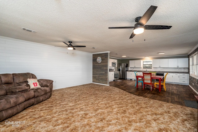 carpeted living room featuring ceiling fan, ornamental molding, and a textured ceiling