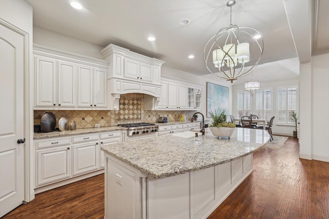 kitchen featuring an inviting chandelier, decorative light fixtures, a kitchen island with sink, and white cabinets