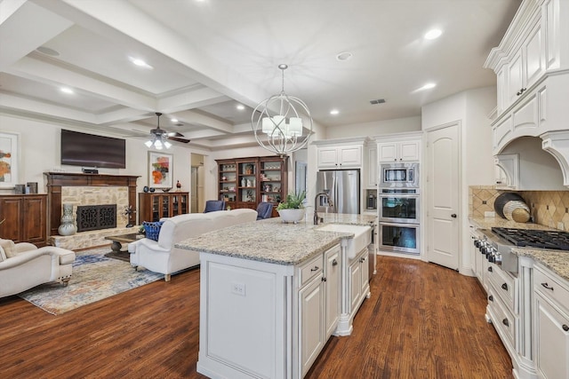 kitchen with white cabinetry, stainless steel appliances, light stone counters, a center island with sink, and decorative light fixtures