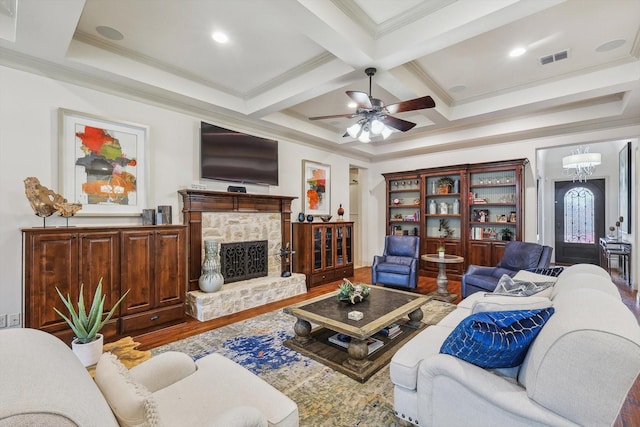 living room featuring a stone fireplace, beamed ceiling, wood-type flooring, ornamental molding, and coffered ceiling