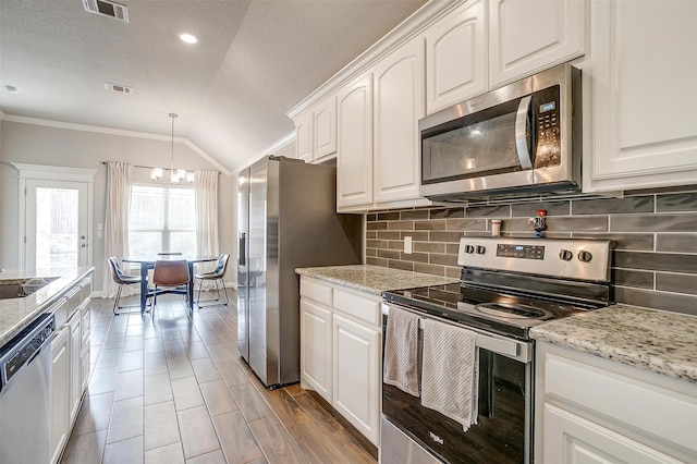 kitchen with appliances with stainless steel finishes, lofted ceiling, white cabinets, hanging light fixtures, and crown molding