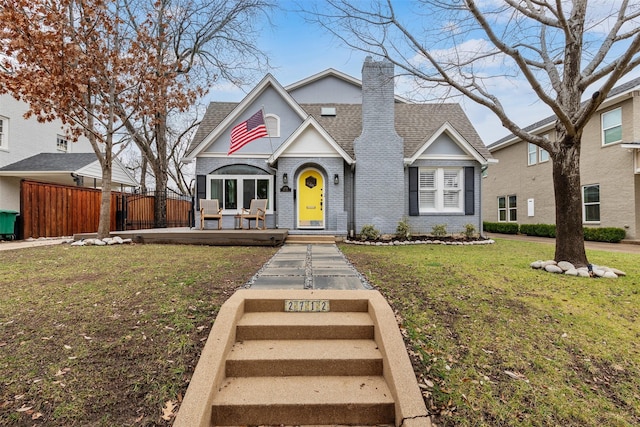 view of front of house featuring fence, roof with shingles, a front yard, brick siding, and a chimney