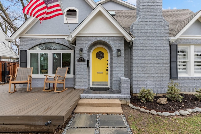 entrance to property featuring fence, roof with shingles, a wooden deck, a chimney, and brick siding