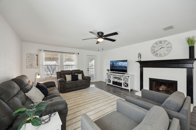 living room featuring dark hardwood / wood-style flooring, a brick fireplace, and ceiling fan