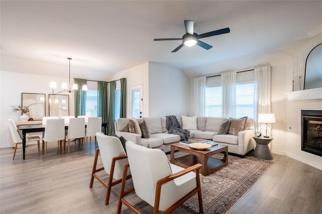 living room with lofted ceiling, ceiling fan with notable chandelier, and light hardwood / wood-style flooring