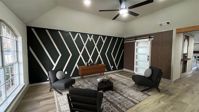 sitting room with vaulted ceiling, a barn door, ceiling fan, and light wood-type flooring