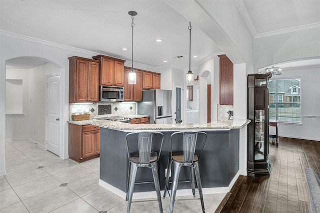 kitchen featuring light stone countertops, hanging light fixtures, stainless steel appliances, and kitchen peninsula