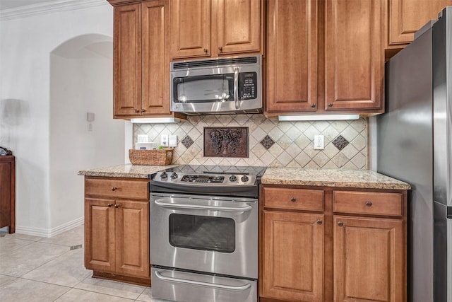 kitchen with light tile patterned flooring, tasteful backsplash, stainless steel appliances, crown molding, and light stone countertops