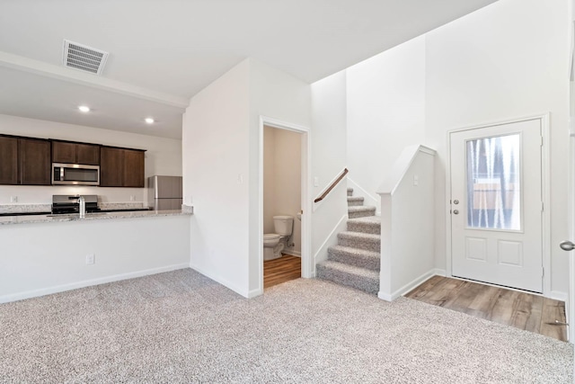 interior space with sink, dark brown cabinets, stainless steel appliances, light stone counters, and light carpet