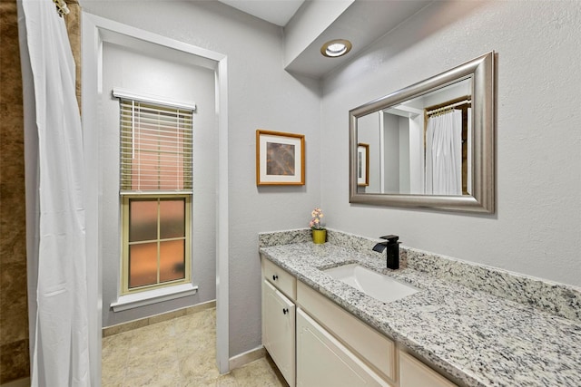 full bathroom with a shower with shower curtain, a textured wall, baseboards, and vanity