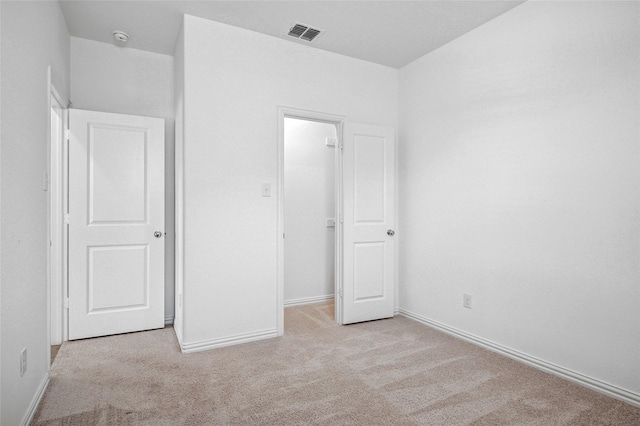 unfurnished bedroom with a walk in closet, light carpet, and a closet