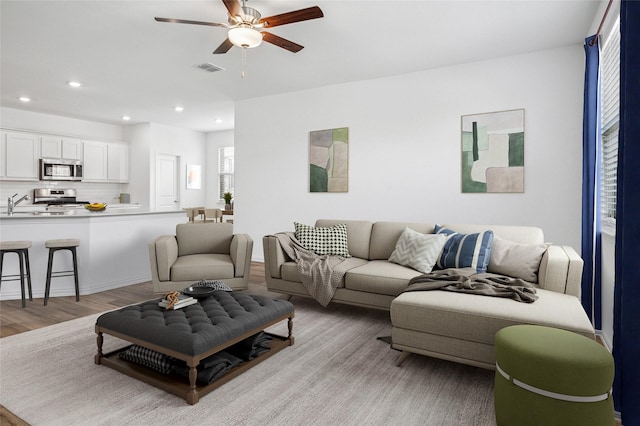 living room featuring ceiling fan, sink, and light hardwood / wood-style flooring