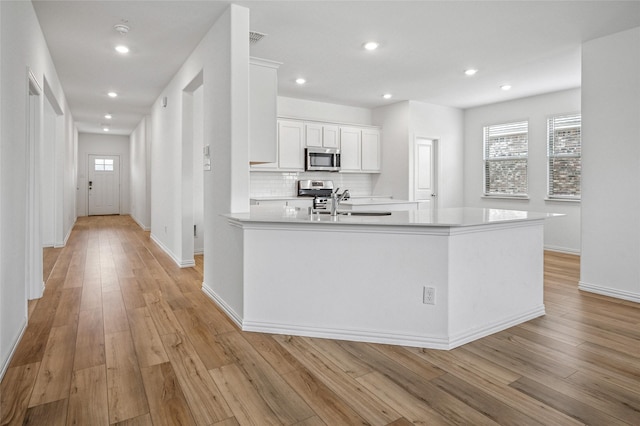 kitchen featuring sink, white cabinetry, stainless steel appliances, light hardwood / wood-style floors, and decorative backsplash