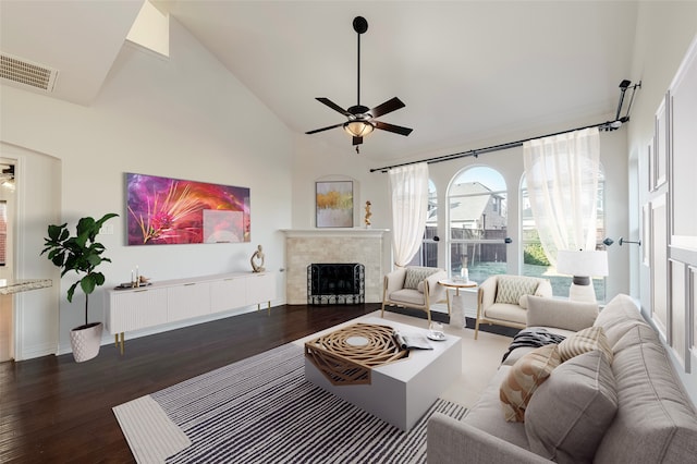 living room featuring dark wood-type flooring, ceiling fan, a tiled fireplace, and high vaulted ceiling