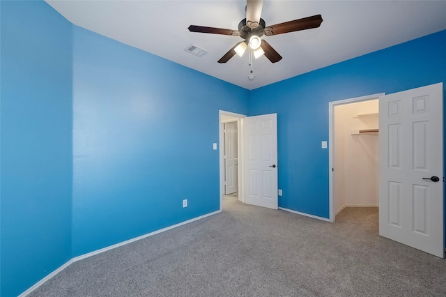 unfurnished bedroom with a walk in closet, light colored carpet, a closet, and ceiling fan