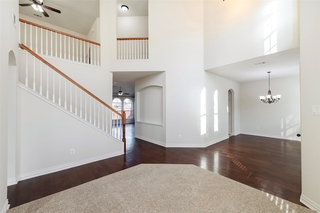 foyer featuring ceiling fan with notable chandelier, dark wood-type flooring, and a towering ceiling