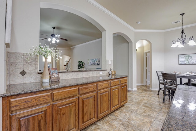 kitchen with tasteful backsplash, crown molding, ceiling fan with notable chandelier, and dark stone counters