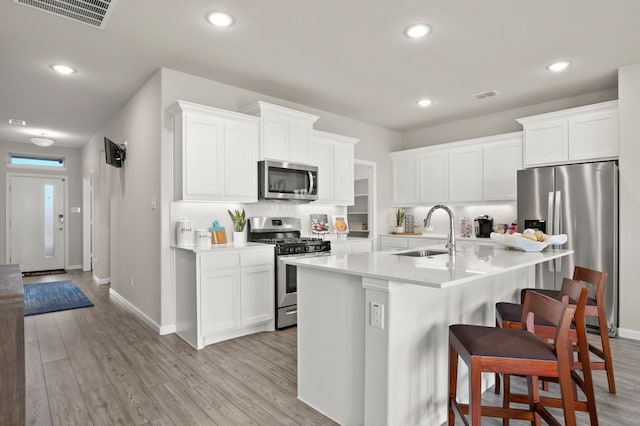 kitchen featuring appliances with stainless steel finishes, sink, a breakfast bar area, white cabinets, and light hardwood / wood-style flooring