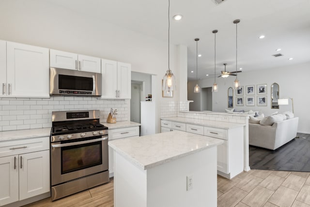 kitchen with a kitchen island, appliances with stainless steel finishes, pendant lighting, and white cabinets