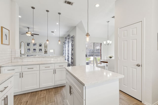 kitchen with white cabinetry, light stone counters, decorative light fixtures, and a center island