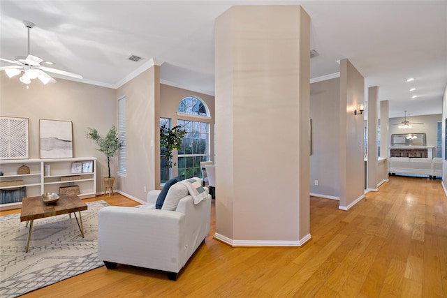 living room featuring ornamental molding, light wood-type flooring, and ceiling fan