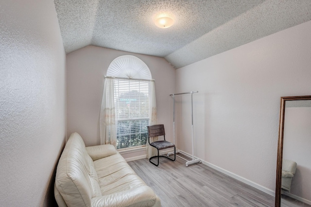 living area with vaulted ceiling, a textured ceiling, and light wood-type flooring