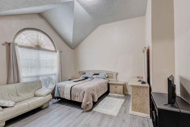 bedroom with vaulted ceiling, a textured ceiling, and light wood-type flooring