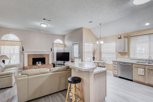 kitchen featuring a breakfast bar, decorative light fixtures, dishwasher, sink, and light wood-type flooring