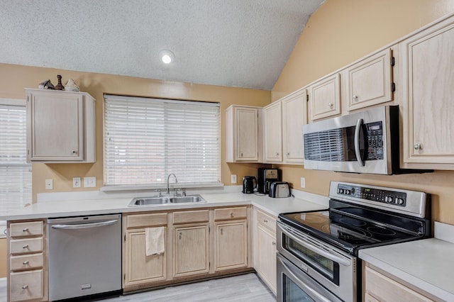 kitchen featuring lofted ceiling, sink, stainless steel appliances, a textured ceiling, and light brown cabinets