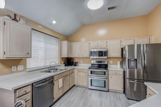 kitchen with lofted ceiling, light brown cabinetry, sink, stainless steel appliances, and light hardwood / wood-style floors