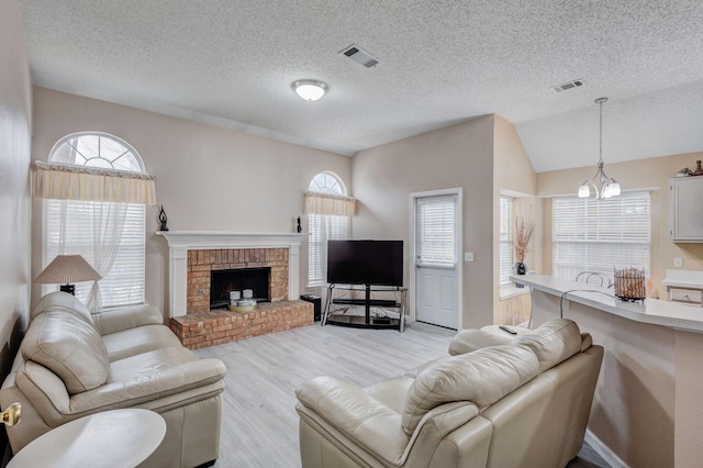 living room featuring a chandelier, vaulted ceiling, a textured ceiling, a brick fireplace, and light wood-type flooring