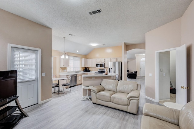 living room featuring sink, vaulted ceiling, a textured ceiling, and light wood-type flooring