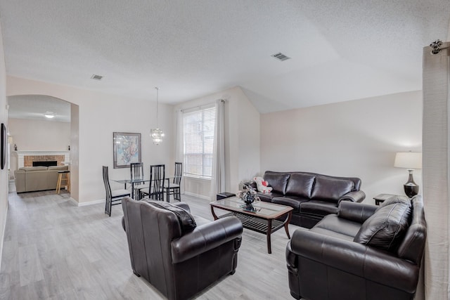 living room with light hardwood / wood-style floors, a brick fireplace, and a textured ceiling