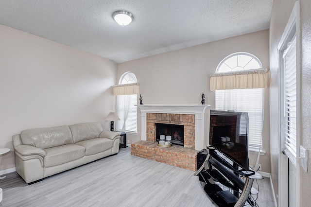 living room featuring a brick fireplace, a textured ceiling, hardwood / wood-style floors, and a healthy amount of sunlight