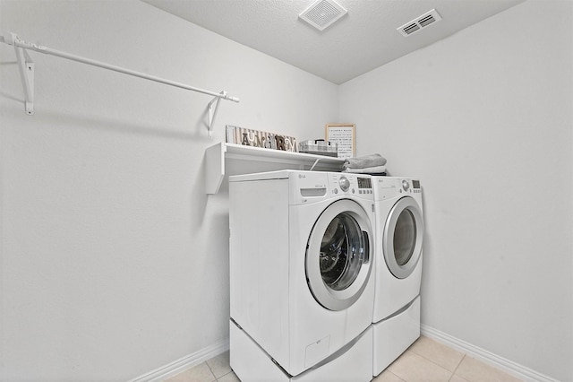 clothes washing area featuring light tile patterned floors, washer and dryer, and a textured ceiling