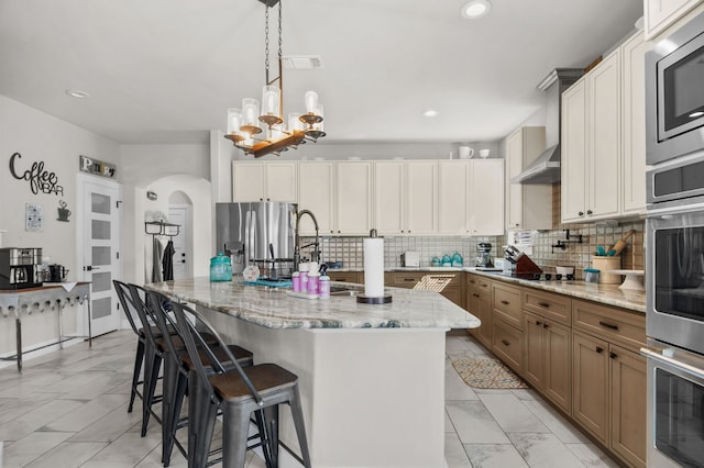 kitchen featuring a large island, appliances with stainless steel finishes, hanging light fixtures, backsplash, and light stone countertops