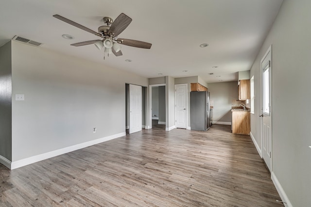 unfurnished living room featuring ceiling fan, sink, and light hardwood / wood-style floors