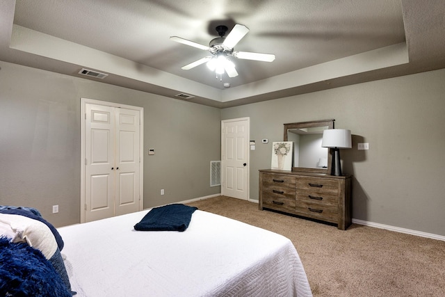 carpeted bedroom with ceiling fan and a tray ceiling