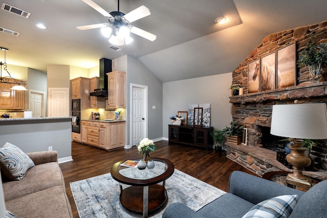 living room with vaulted ceiling, a stone fireplace, ceiling fan, and dark hardwood / wood-style flooring