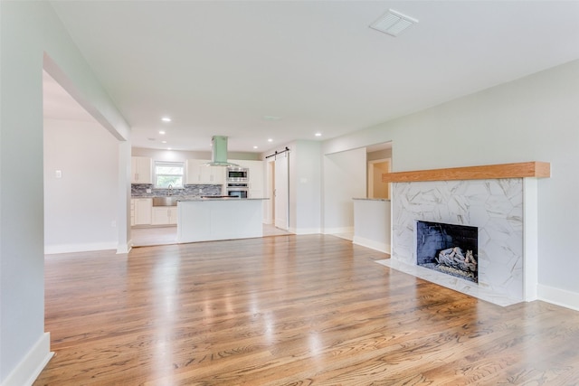 unfurnished living room featuring a fireplace, light hardwood / wood-style floors, and a barn door