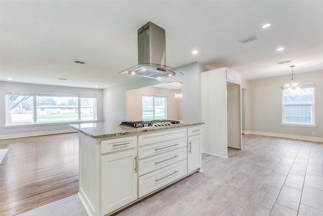 kitchen featuring a center island, light stone countertops, white cabinets, island exhaust hood, and stainless steel gas stovetop