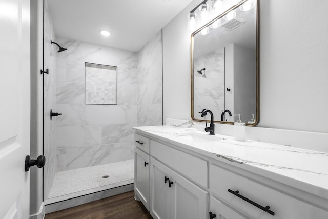 bathroom featuring wood-type flooring, a tile shower, and vanity