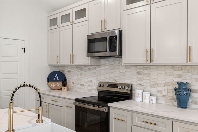 kitchen featuring sink, white cabinetry, light stone counters, appliances with stainless steel finishes, and decorative backsplash