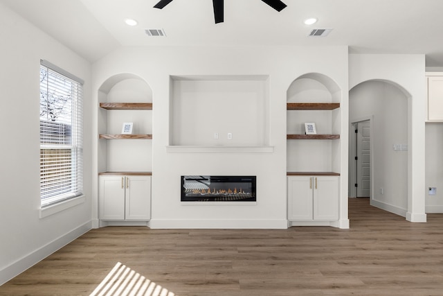 unfurnished living room featuring built in shelves, ceiling fan, and light hardwood / wood-style floors