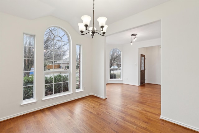 unfurnished dining area featuring hardwood / wood-style flooring, lofted ceiling, and a chandelier