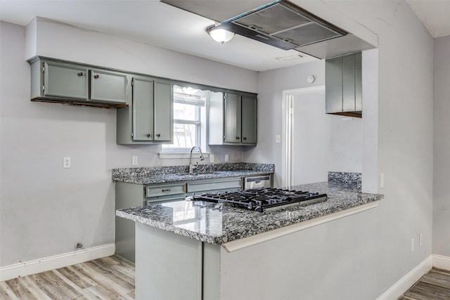 kitchen featuring sink, dark stone countertops, light hardwood / wood-style floors, kitchen peninsula, and stainless steel appliances