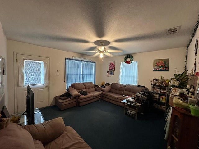 living room featuring dark colored carpet, ceiling fan, a textured ceiling, and a wealth of natural light