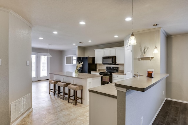 kitchen with a breakfast bar area, black appliances, hanging light fixtures, kitchen peninsula, and white cabinets